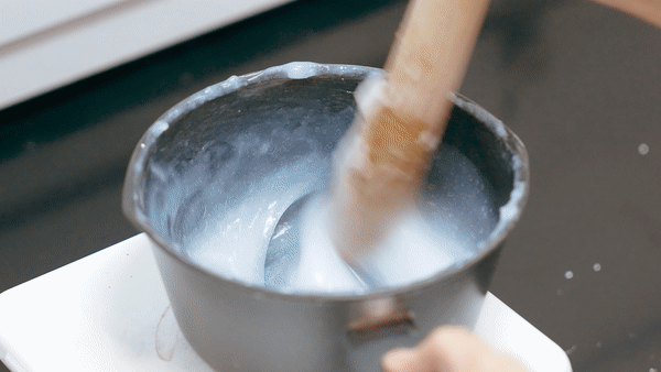 Close-up of a wooden paddle actively stirring white starch in a pot, the motion captured in the looping animation. 