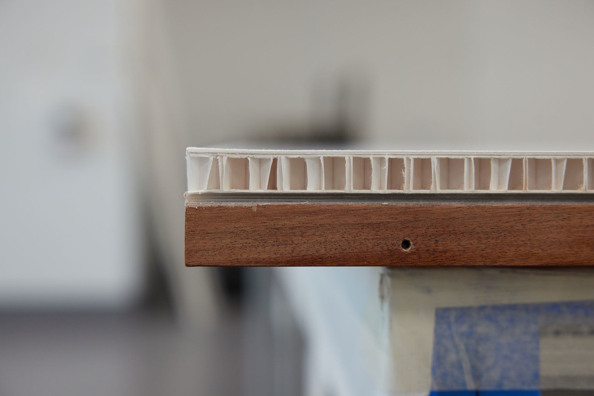 A side view of a honeycomb board reveals its tightly packed hexagonal cells, forming a rigid structure. The board rests evenly atop a wooden lattice framework below.