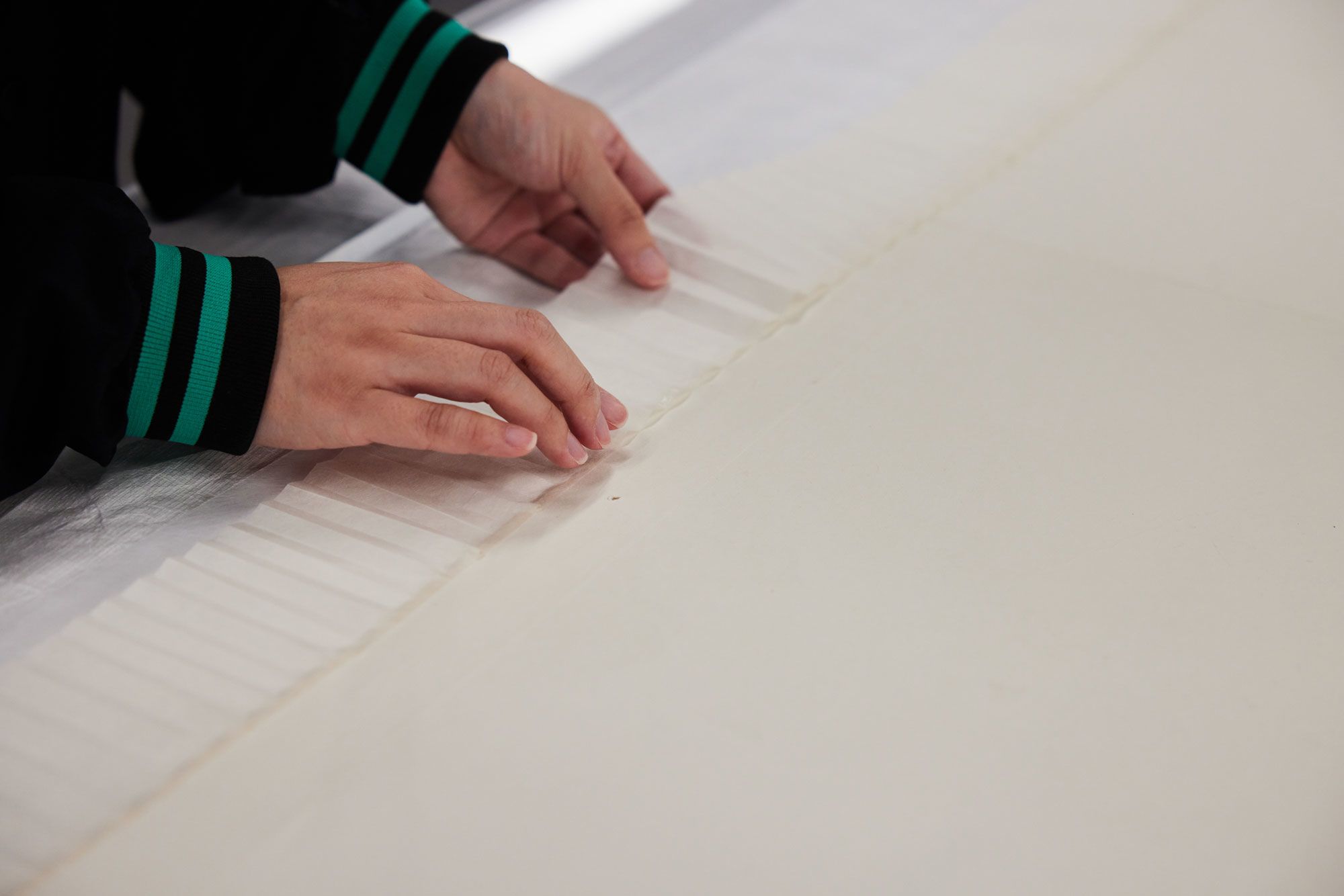 Two hands delicately position strips of Japanese ‘kozo’ paper along the margin of an artwork.
