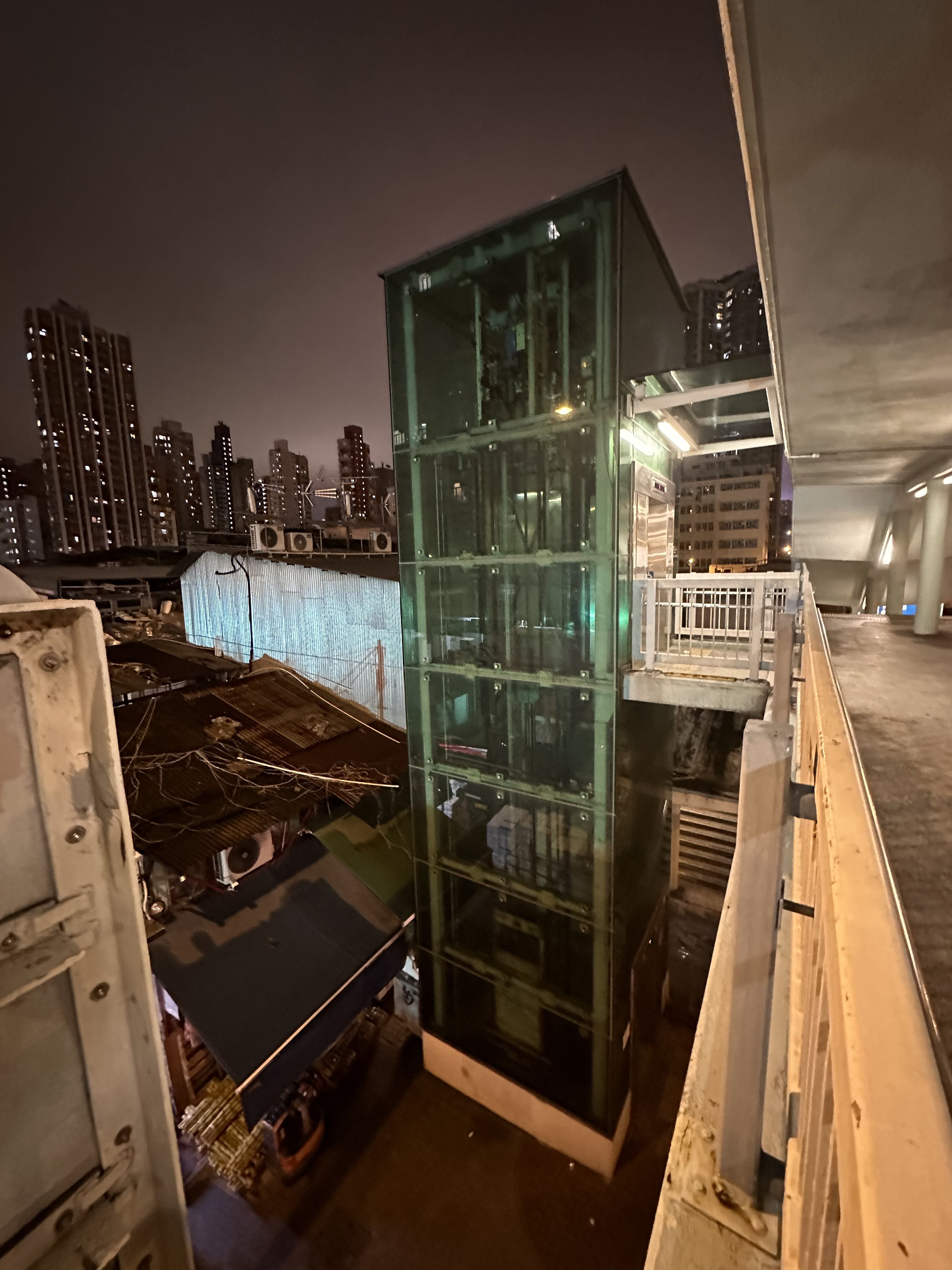 从行人天桥拍摄一部在铁皮屋顶水果摊档旁的玻璃升降机槽。