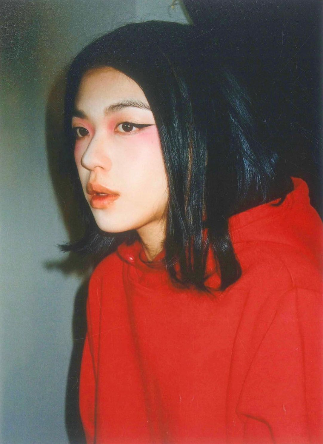 一个化了浓浓眼妆的人，目光离开镜头；画面被闪光灯照亮。