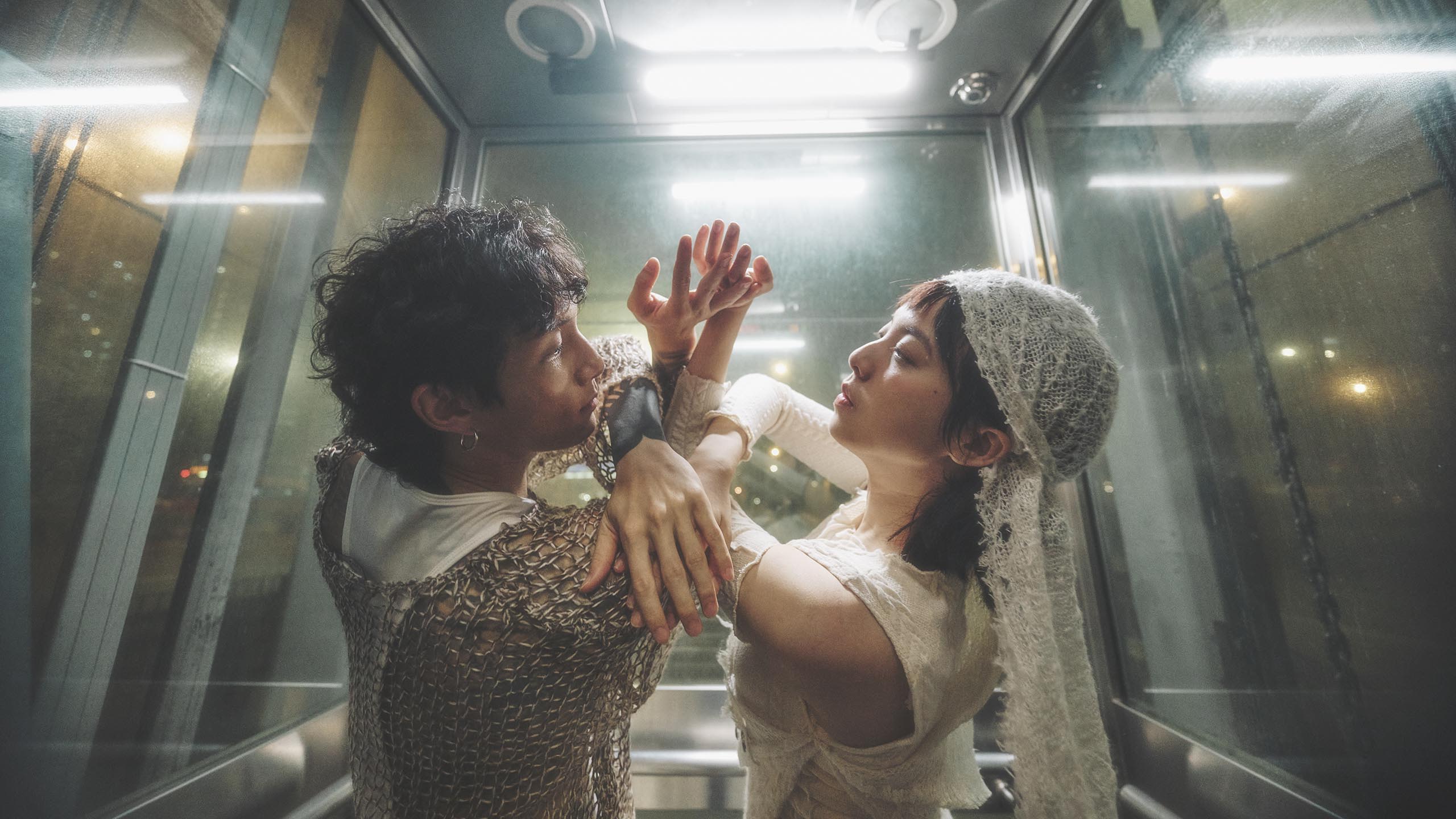 两位表演者在晚上于一部发光的升降机内跳舞。