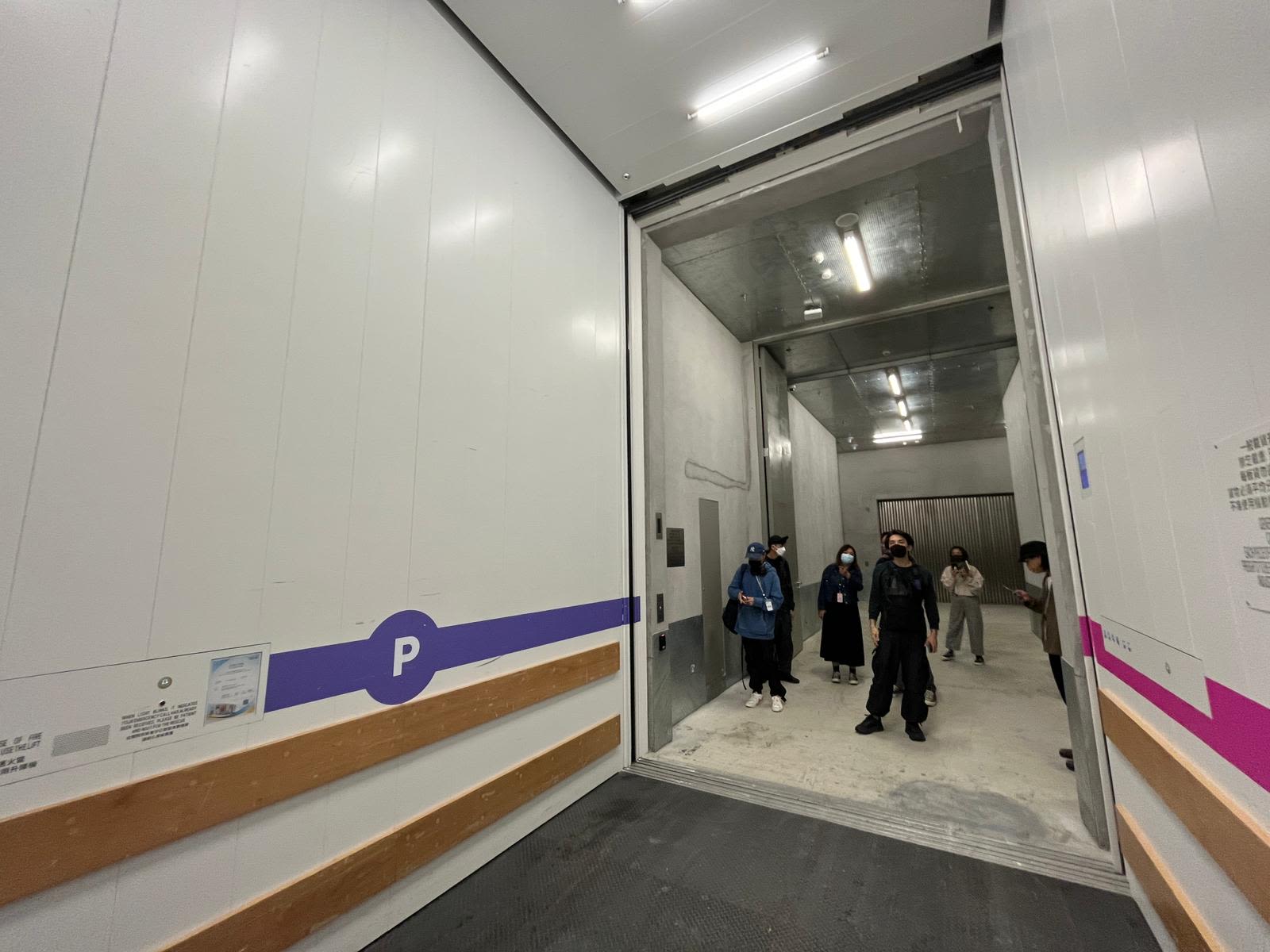 一群人看着一部载货升降机，这台设有白墙的升降机天花板十分高。