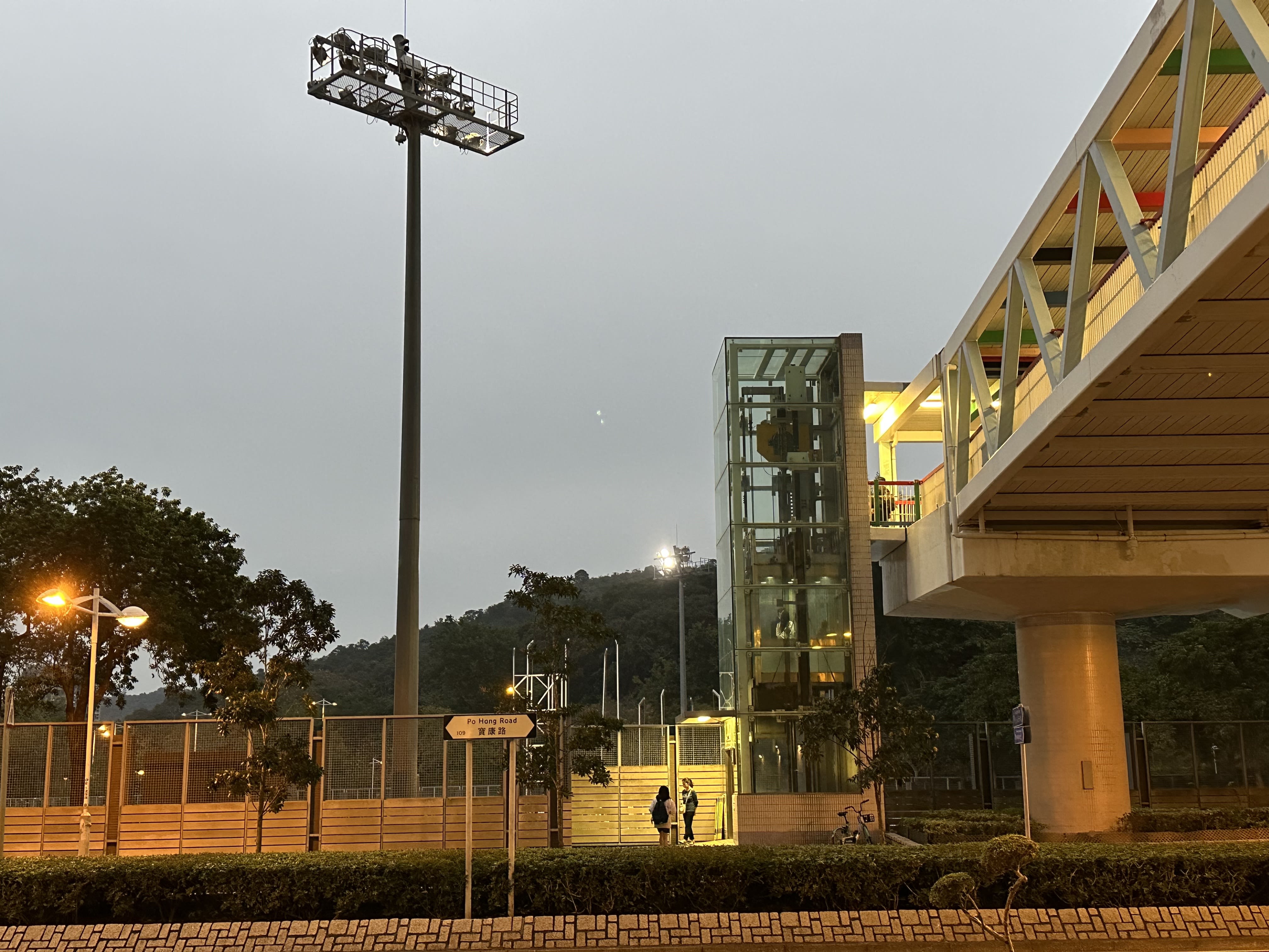 从街道拍摄的一部连接行人天桥的升降机，远处可见绿色的山。