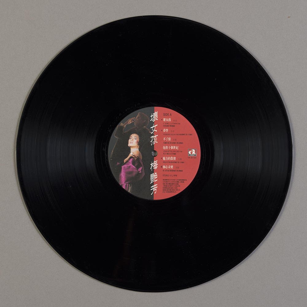 梅艳芳《坏女孩》12吋黑胶唱片的A面，白色直书的标题在唱片标签的中央位置。左方可见两个重叠的梅艳芳肖像，分别穿上紫色缎面裙和外套。右方则见红色背景，上面印有曲目。
