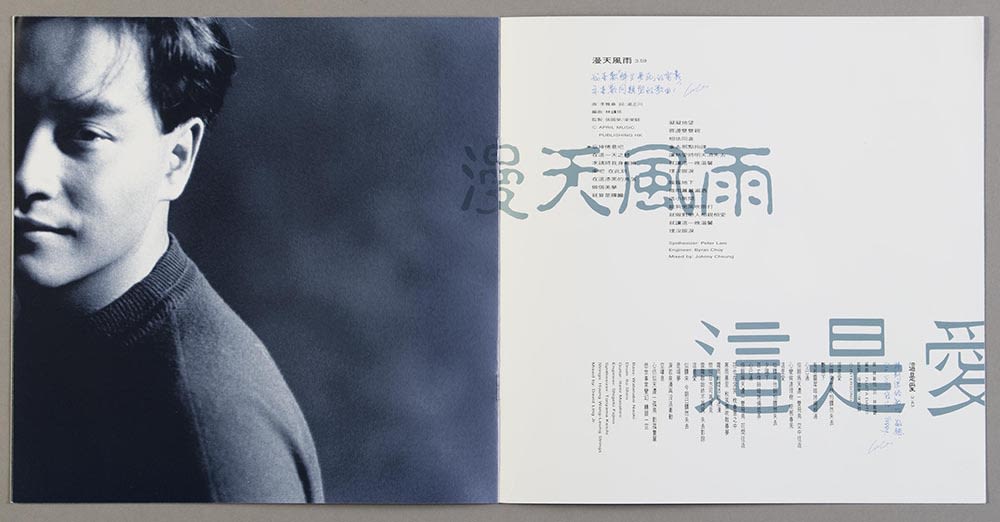 张国荣《Salute》镭射唱片歌词小册子跨页。左页有张国荣的黑白正面照，画面只见半张脸。右页可见两首歌的歌词，浅蓝色的歌名和黑色的歌词以直书及横书方式排列。