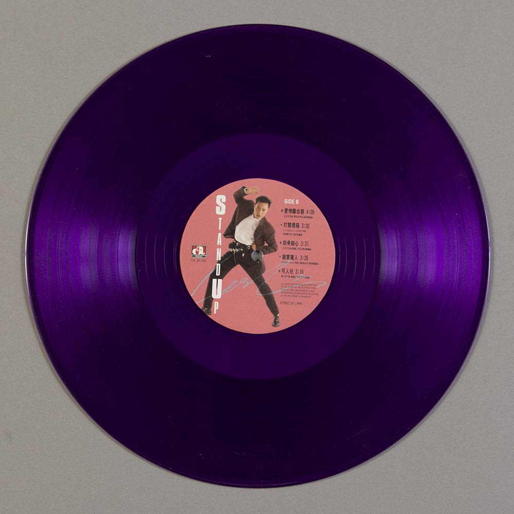张国荣《Stand Up》12吋紫色黑胶唱片B面。白色直书标题在唱片标签左方。标签的粉红色背景上可见张国荣身穿白色衬衫、棕色外套和黑色长裤；右方则印有曲目。