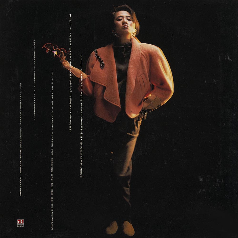 梅艳芳《坏女孩》黑胶唱片封底。黑色背景上，梅艳芳站在中央，身穿橙红色外套，右手拿着一副太阳眼镜。封底左方可见白色直书的曲目及唱片资料。