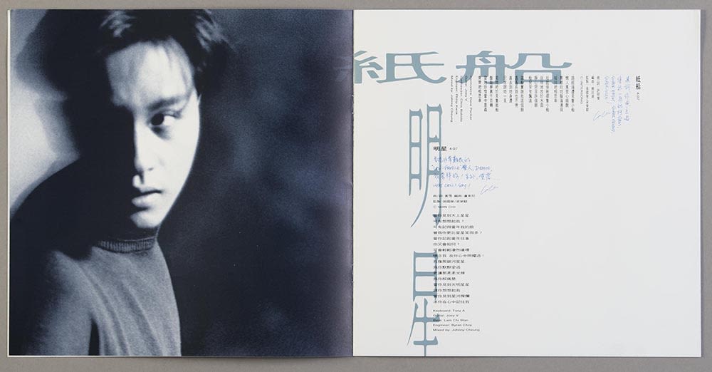 张国荣《Salute》镭射唱片歌词小册跨页。左页有张国荣的黑白正面照，画面只见大半张脸。右页可见两首歌的歌词，浅蓝色的歌名和黑色的歌词以直书及横书方式排列。