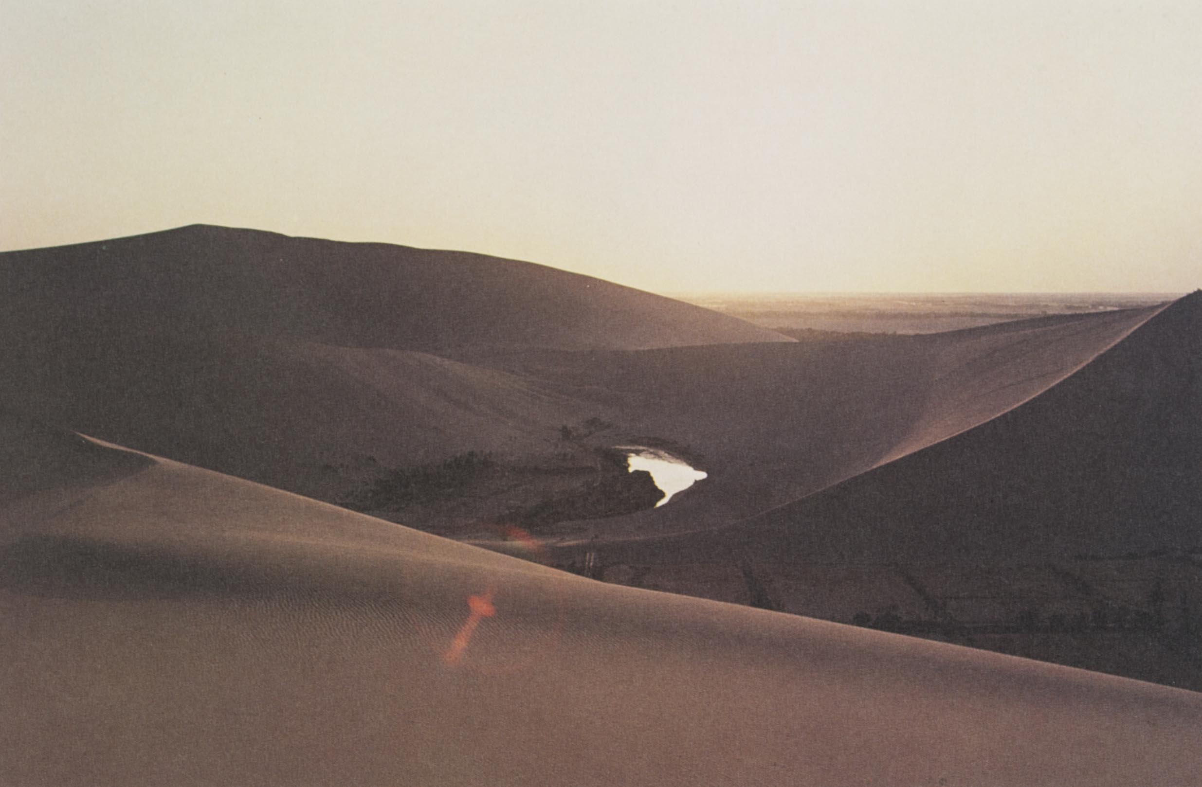 Detail of a square postcard gifted with the Silk Road Tour: Music Collection vinyl album, featuring a photograph of the Mingsha Mountain with the Crescent Moon Spring in the middle. 