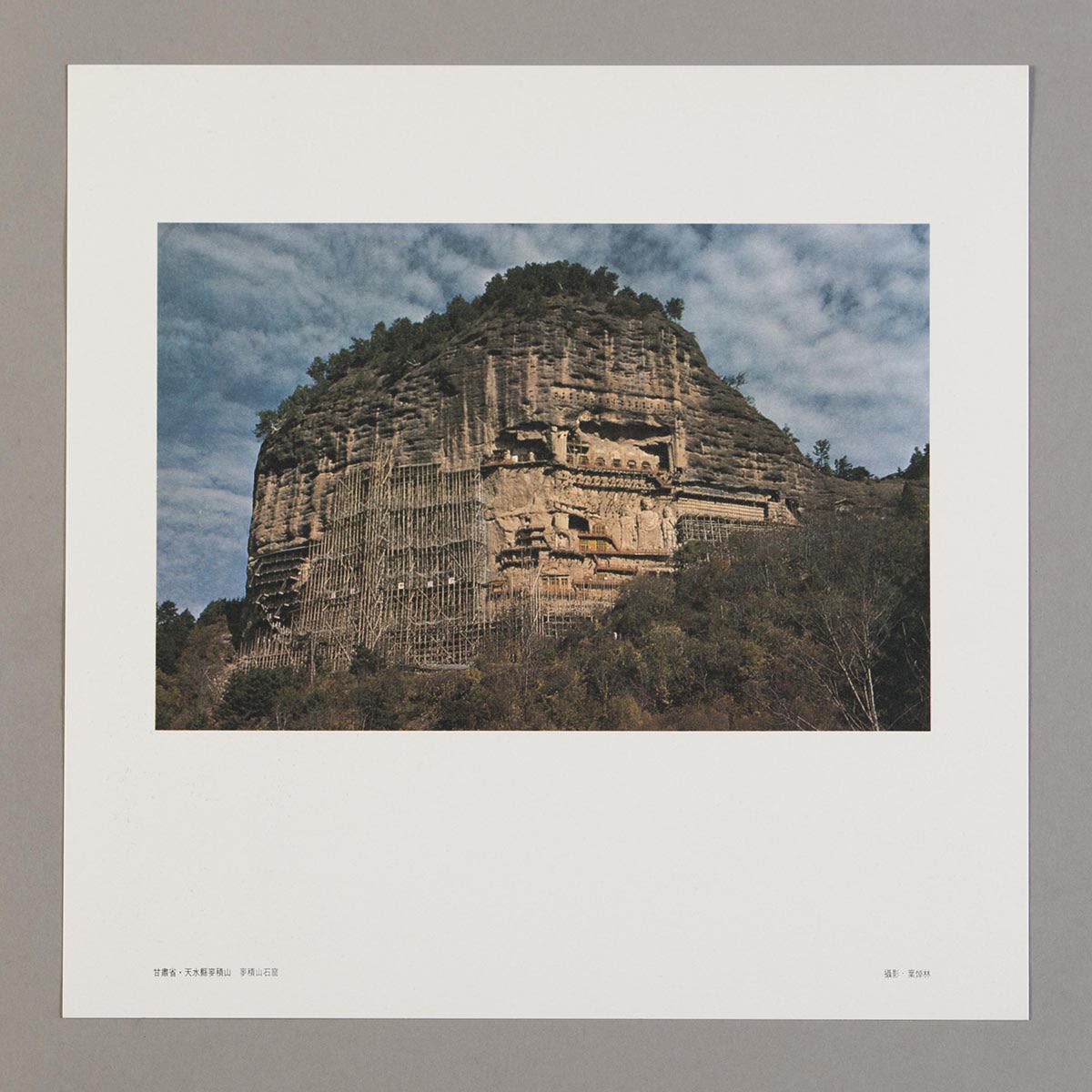 随《丝绸之路巡礼名曲集》黑胶唱片所附送的长方形明信片。白色边框内的照片可见麦积山石窟及布满云朵的蓝天。