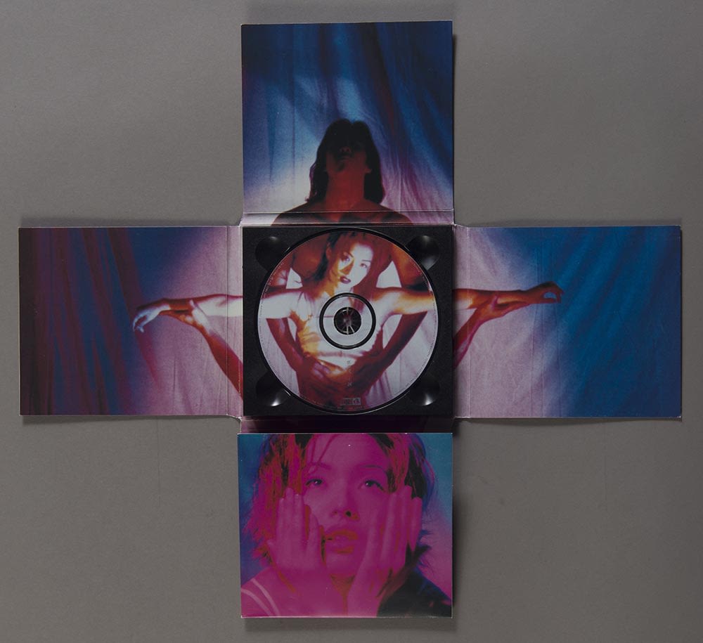 郑秀文《十诫》镭射唱片封套内页，摊开了的纸套呈十字架形状。紫红色和蓝色色调的照片带有颗粒效果。郑秀文直视镜头，双臂往左右直伸。两名男子分别在她身后和下方，一人将她环抱，一人把她举起，形成十字架的姿势。