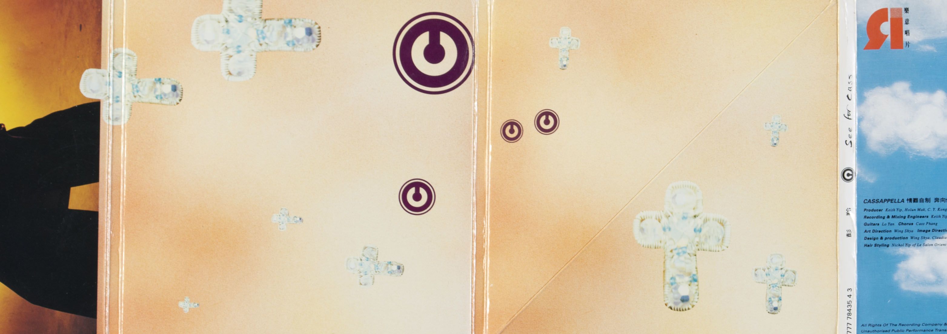 Interior view of Cass Pang’s CD album See for Cass. The two-page spread has a coral background, decorated with four circular stamps of the letter ‘c’ in wine red and nine white beaded crosses. 