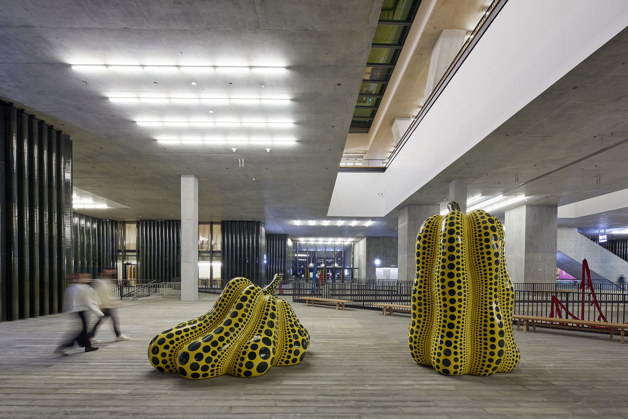 Two sizeable yellow pumpkin sculptures, one squat, one tall, featuring vertical strips of black polka dots along their shells.