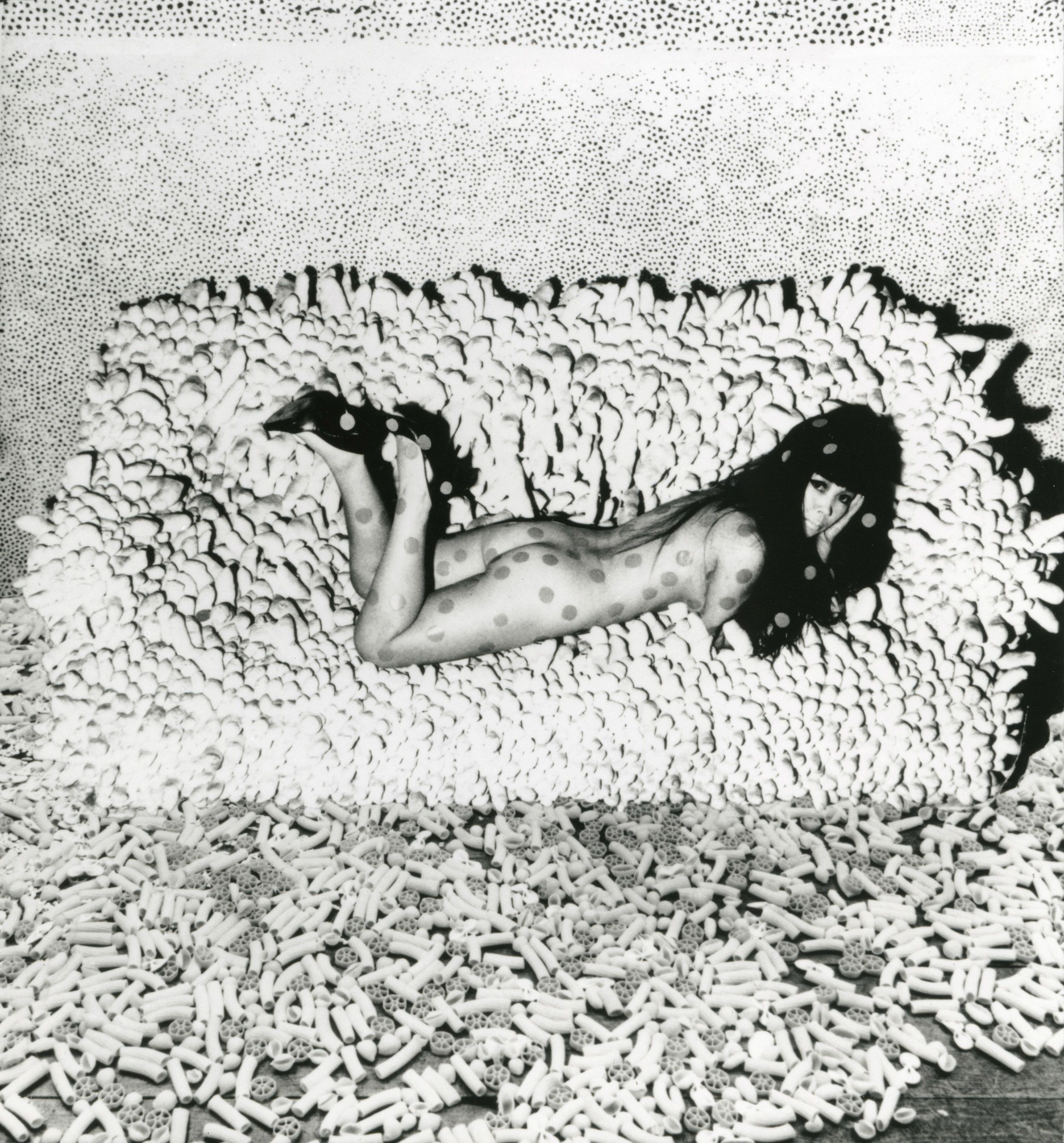 黑白照片中，草间弥生俯卧在一张背靠墙壁的沙发上。整张沙发的表面被突出状填充织物包裹着，墙壁上满布繁复盘绕的圆环网纹。艺术家留着长长的黑发，身上布满圆点，俯卧着并两膝屈曲，脚尖朝上。不同形状的通心粉于前景撒满一地。