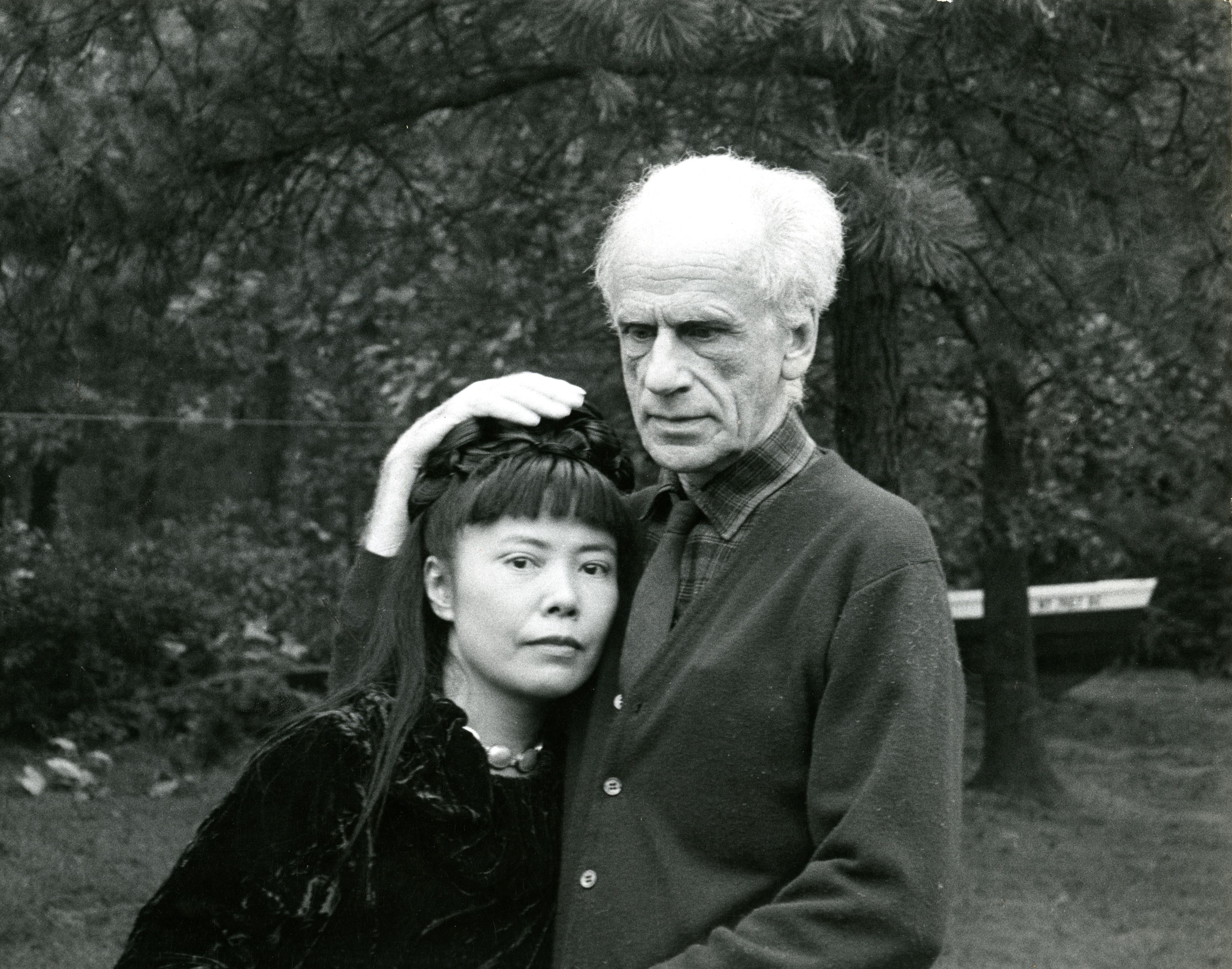 黑白照片中是约瑟夫·康奈尔和草间弥生，草间靠在康奈尔的胸膛，而康奈尔的手放在草间头上。他们身后可见树木枝叶。