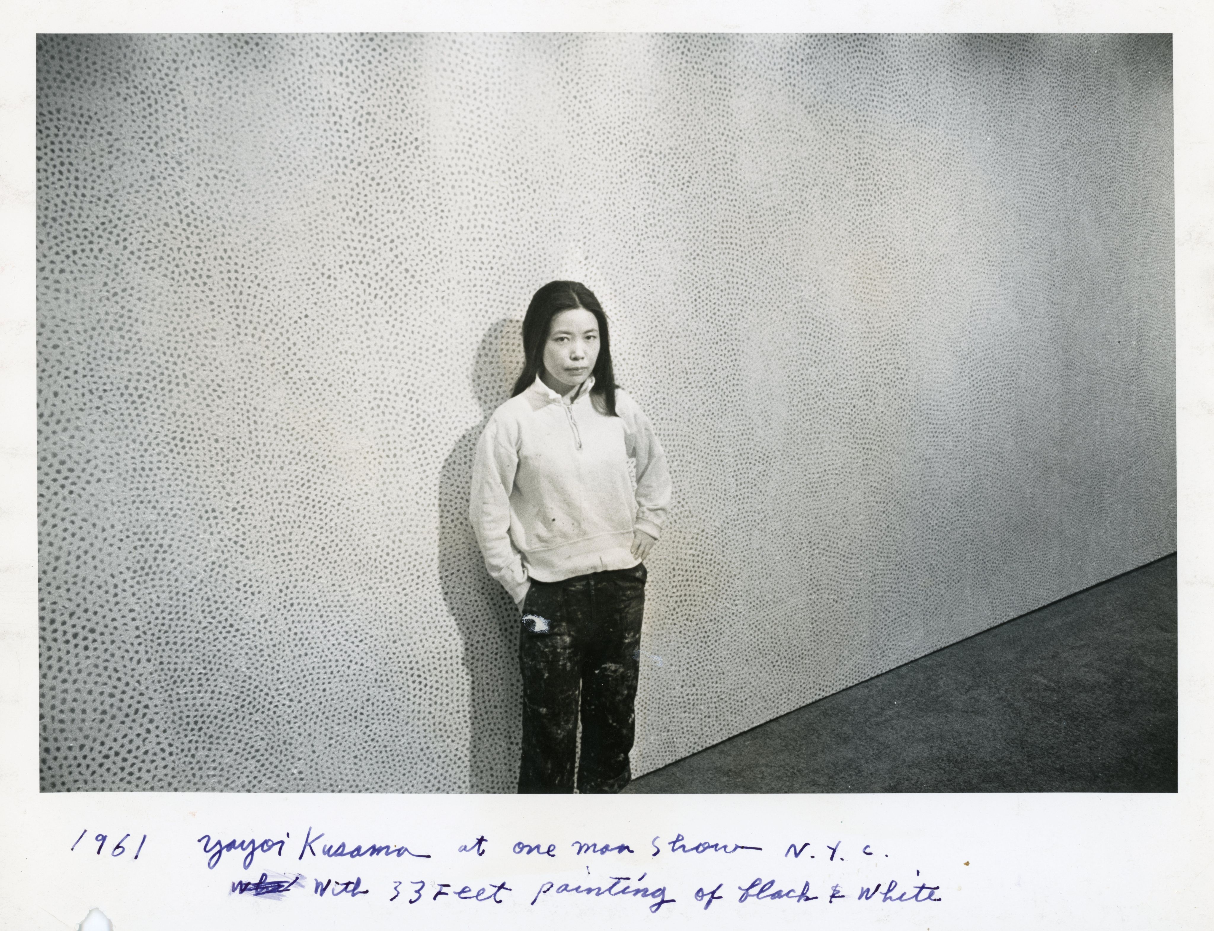 黑白照片中，草间弥生站在其十米长的画作《无限的网》前。她身穿白色上衣和沾染颜料的黑色工装裤。照片底部以蓝色墨水写上「1961年草间弥生于纽约个展，身后为三十三呎长的黑白画作」。