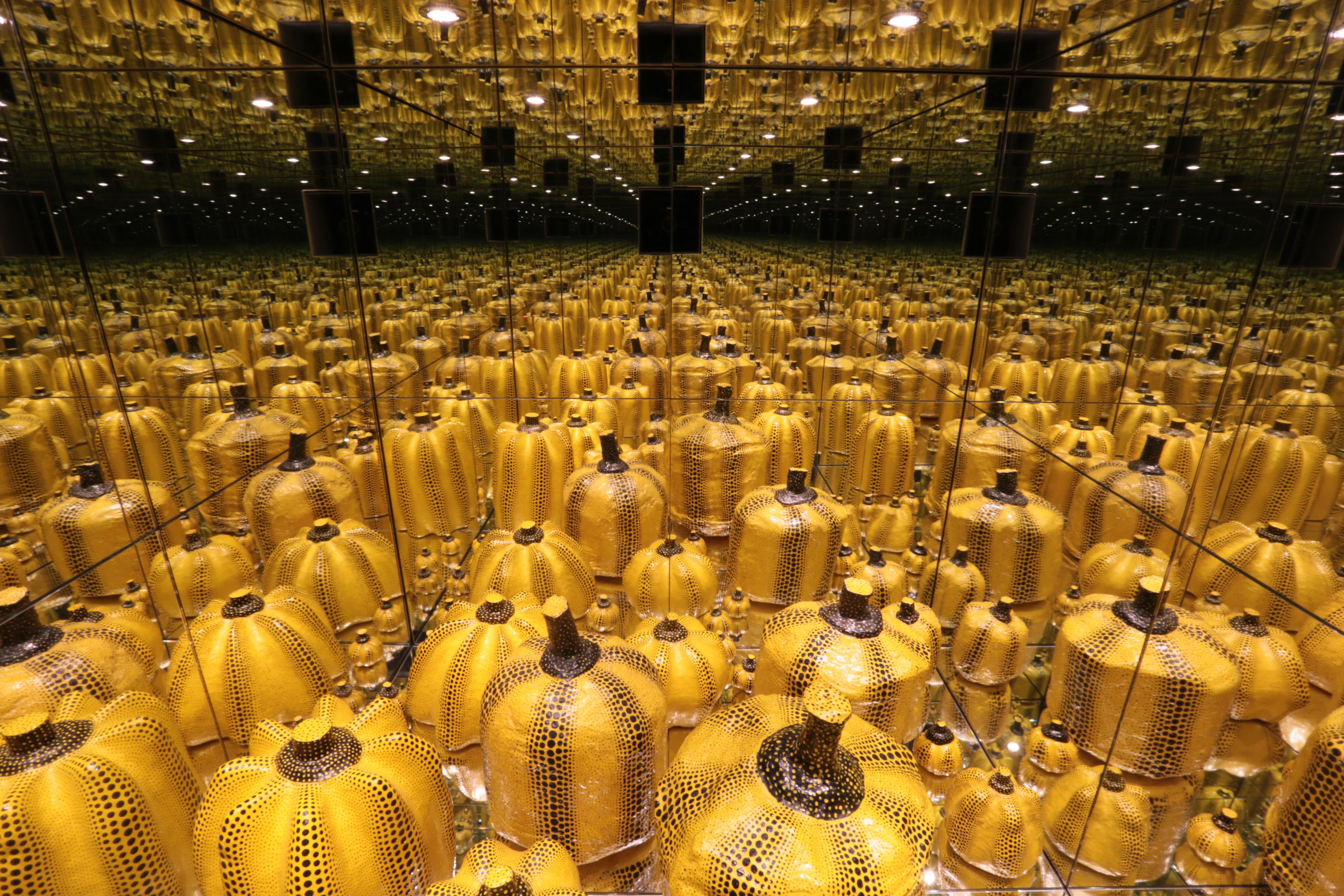 装置作品中，各种形状和大小的黑点黄色南瓜雕塑置于镜室地面，形成了一条无穷无尽的倒影隧道。