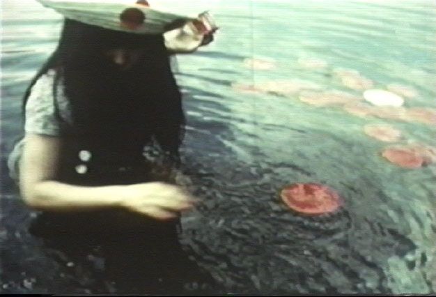 电影截图中的女子是艺术家草间弥生。她半身浸没在一个看似湖泊的地方，水深齐腰，正在观察漂浮在水面上的红色圆点。